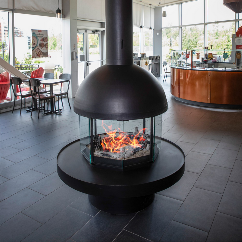 Modern black freestanding fireplace with flames inside, set against a restaurant interior.