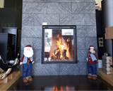 Gray stone fireplace with mounted deer antlers and two Santa Claus figurines in a room.