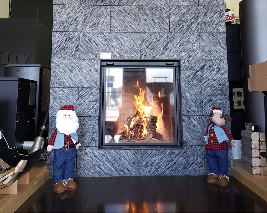 Gray stone fireplace with mounted deer antlers and two Santa Claus figurines in a room.